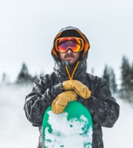 Johan står i snowboardkläder med skidglasögon lutandes med kroppen på sin snowboard