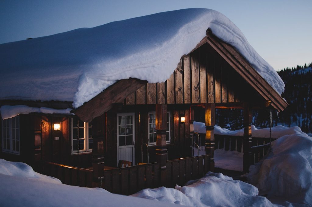Stuga med snöig uteplats i skymning.