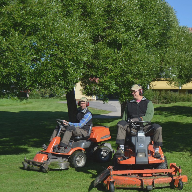 Två medarbetare klipper gräs med åkgräsklippare